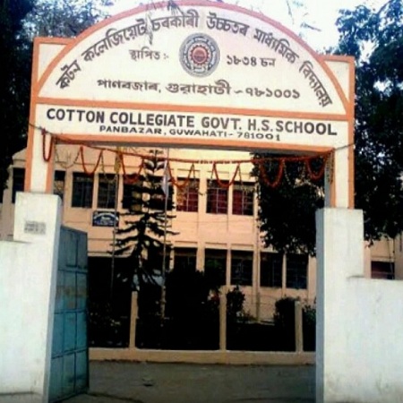 Entrance gate of Cotton Collegiate Government Higher Secondary School in Panbazar, Guwahati, showing a white arch with English and Assamese signage and a multi-story school building inside.